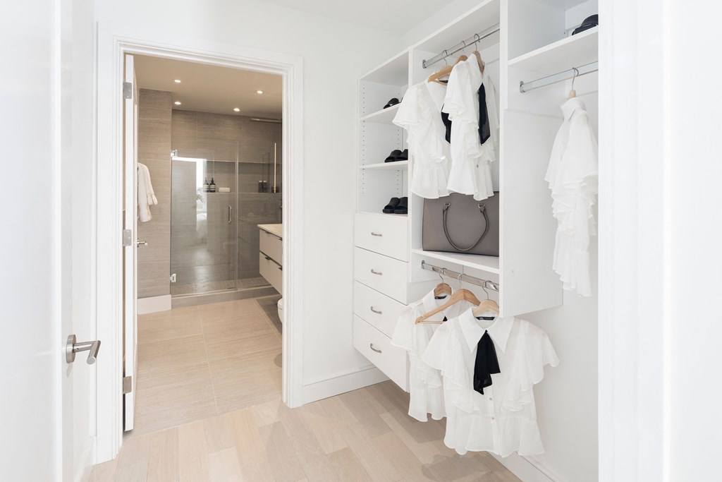 a walk in closet with white cabinets and a closet door open to a white wardrobe