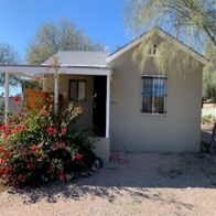 a small white house with a porch and a tree