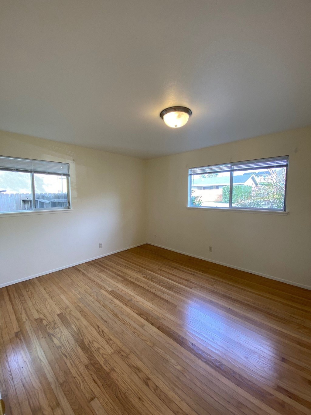 the living room of an empty house with wooden floors and two windows