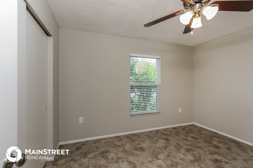 the spacious living room of this home has a ceiling fan and a window