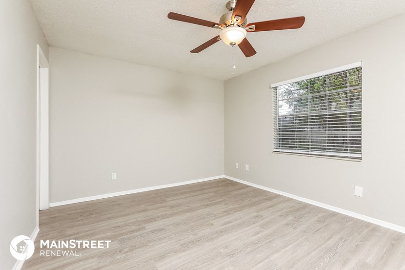 the spacious living room with a large window and a ceiling fan