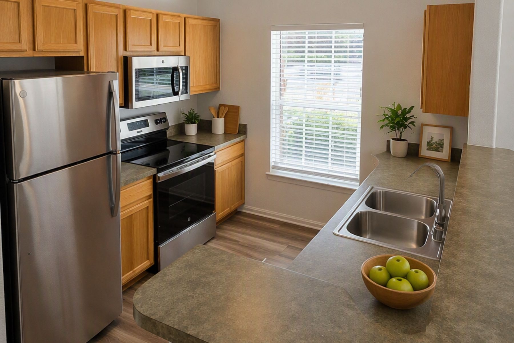 A kitchen with a refrigerator, microwave, oven, sink, and a bowl of apples on the counter.