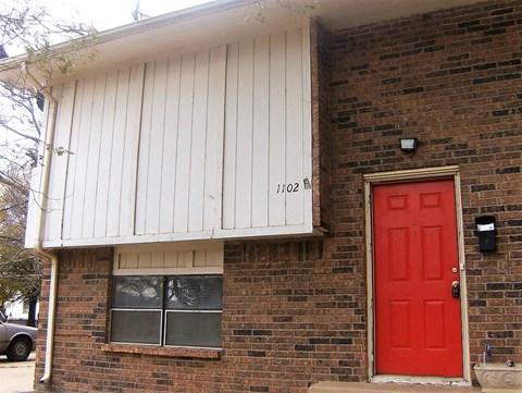 A red door is on the right side of a brick house.