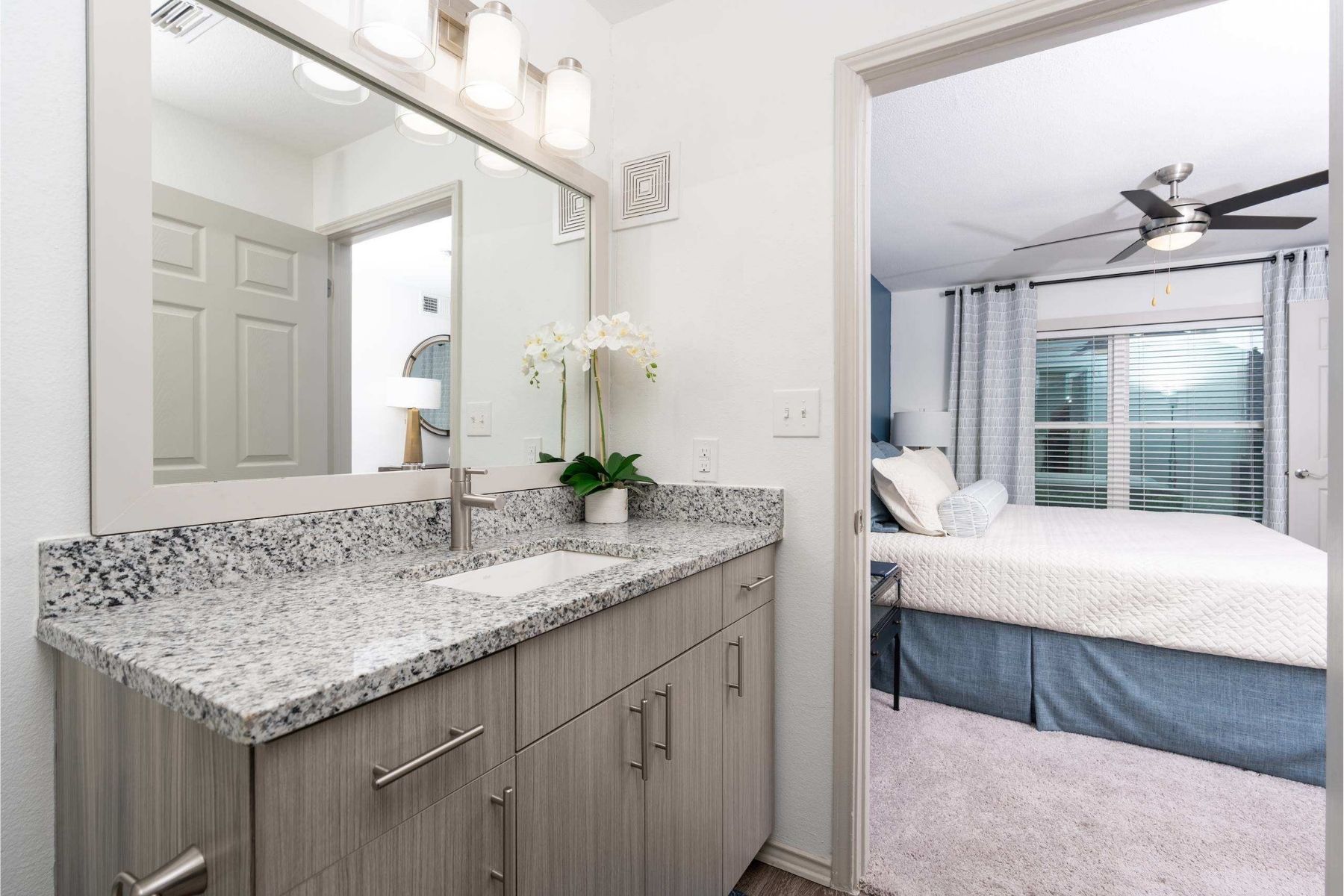 A bathroom with a marble countertop and a bedroom with a bed and a ceiling fan.