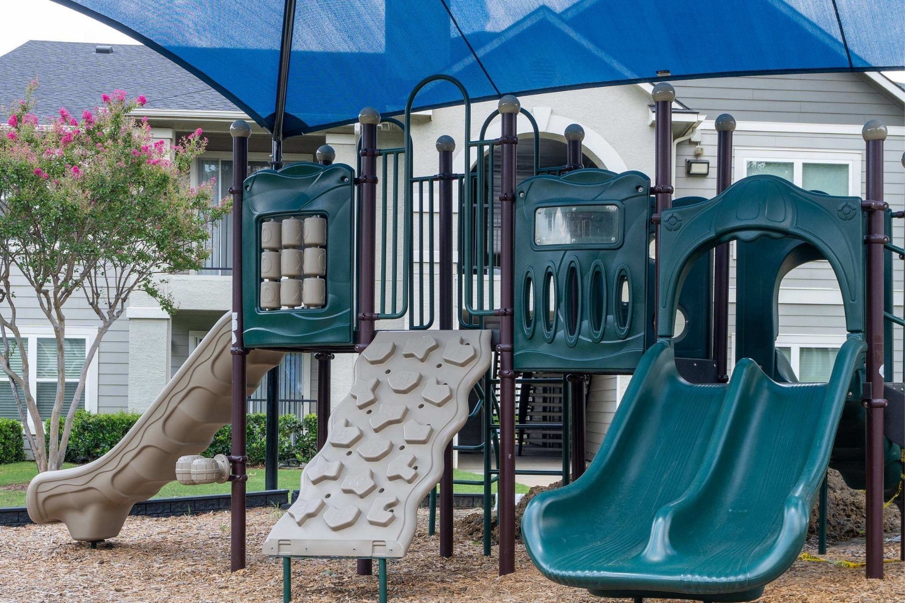 A playground with a green slide and a brown sandbox.