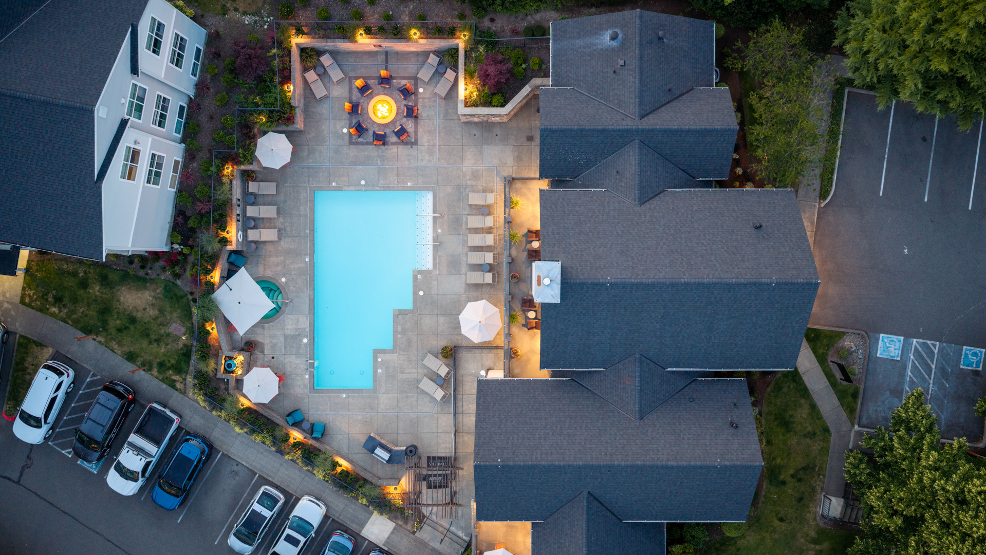 A pool surrounded by a patio with chairs and a fire pit.