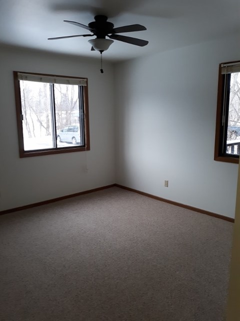 A room with a ceiling fan and two windows.