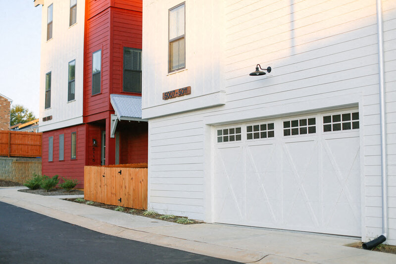 a white house with a white garage door in front of a red building