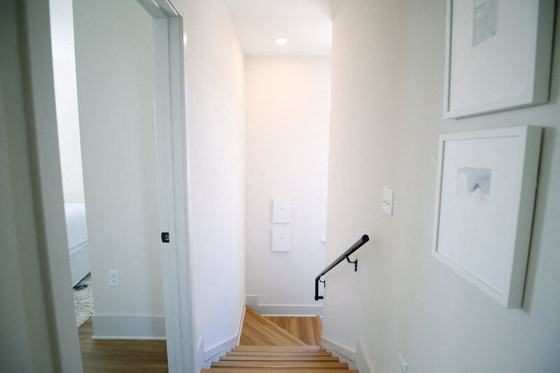 a hallway with stairs and a white wall and a black hand rail