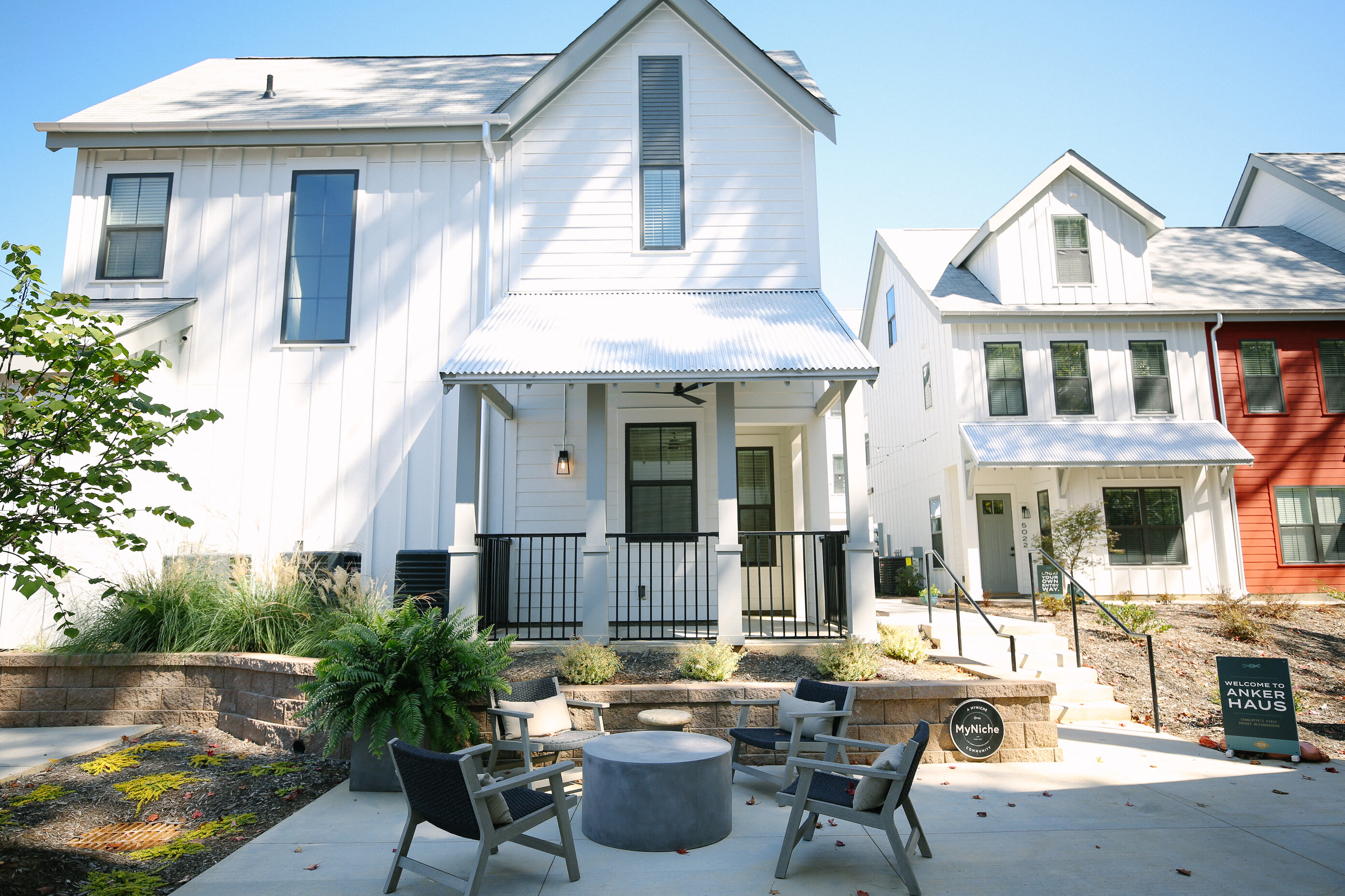 a patio with chairs and tables in front of a white house