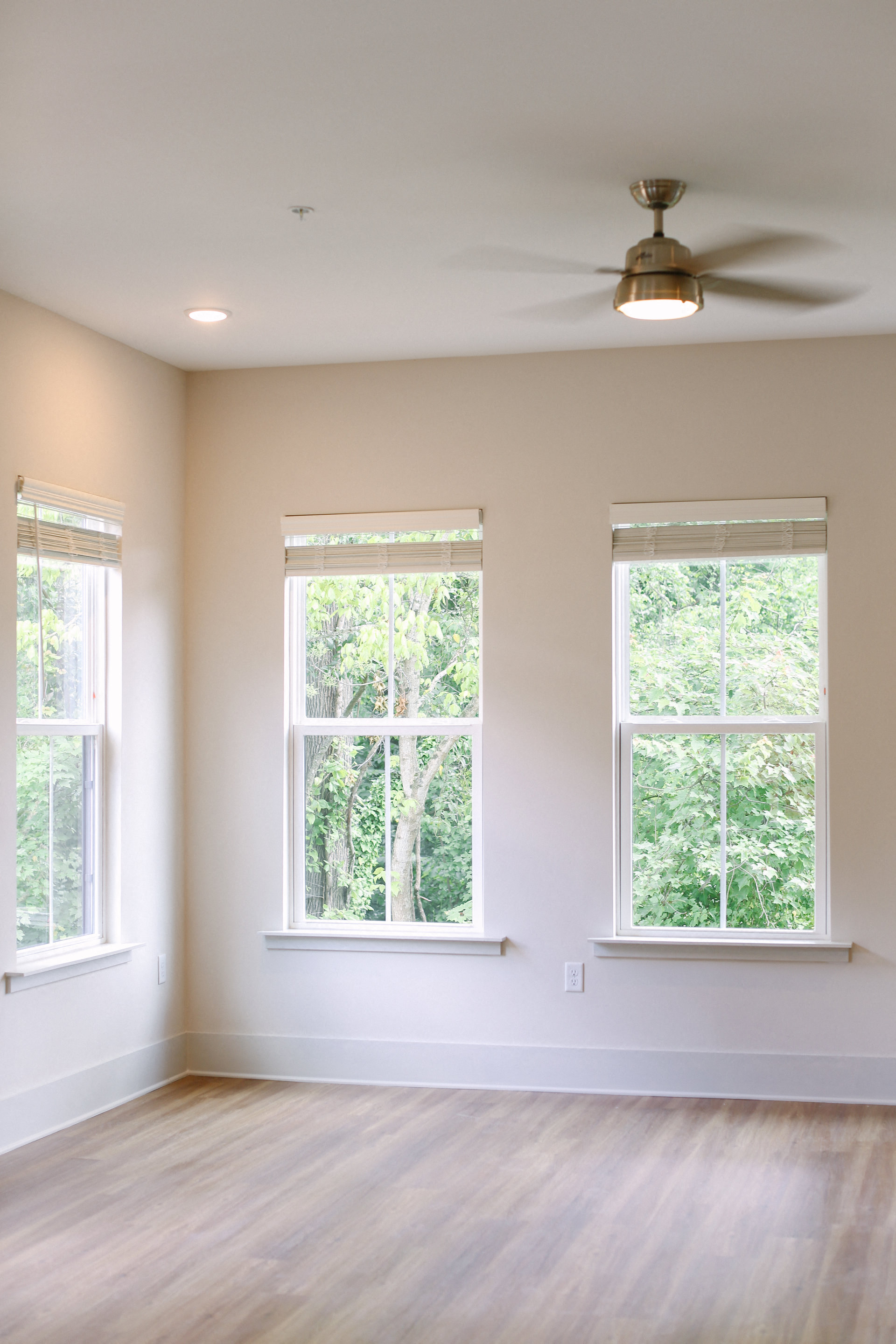 an empty room with three windows and a ceiling fan