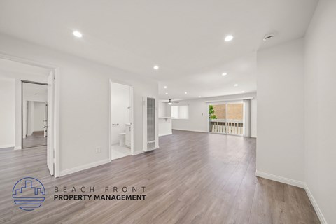 A spacious room with wooden floors and white walls, with a logo for Beach Front Property Management in the bottom left corner.