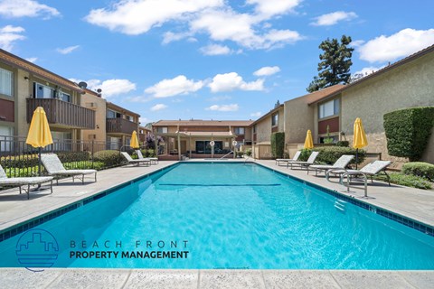 A swimming pool surrounded by sun loungers and umbrellas in a residential area.