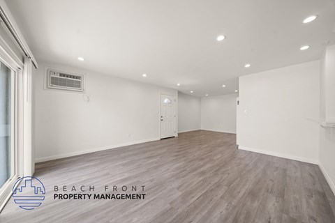 A spacious room with wooden flooring and white walls, featuring a large window and a mounted air conditioning unit.