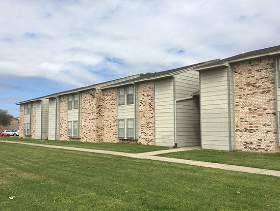 an apartment building with gray and white siding and a green lawn