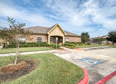 the front of a brick house with a parking lot and grass