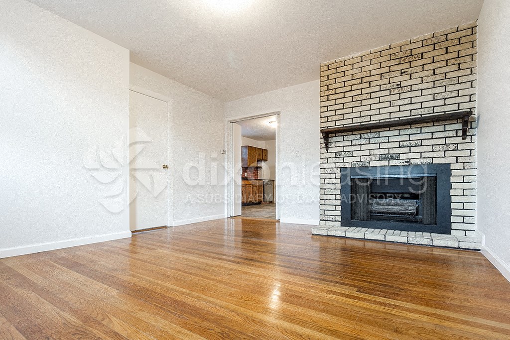 a living room with a brick fireplace and wooden floors
