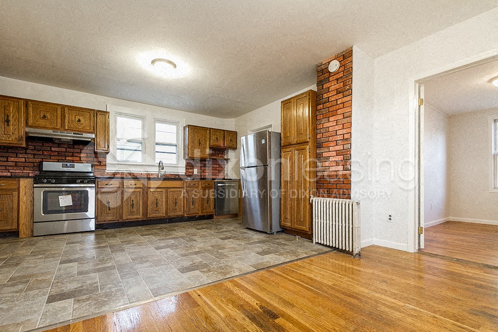 a kitchen with a brick wall and wooden cabinets and a stainless steel refrigerator