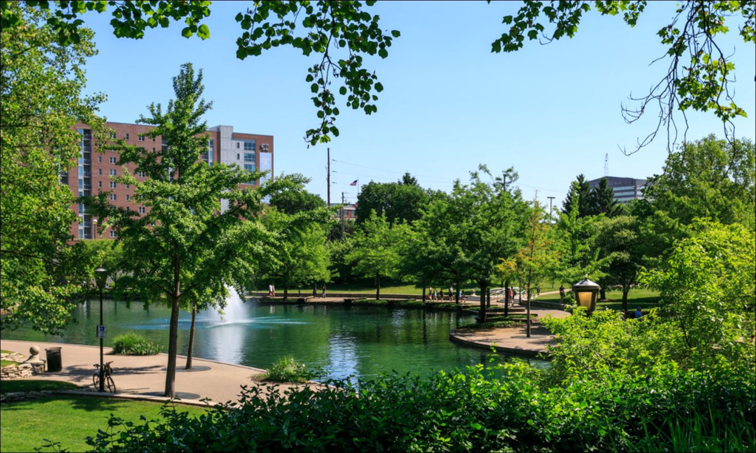 a pond in the middle of a park with trees and buildings