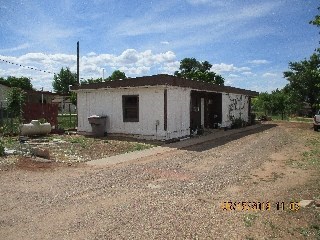 A small white building with a brown roof is surrounded by a dirt area.