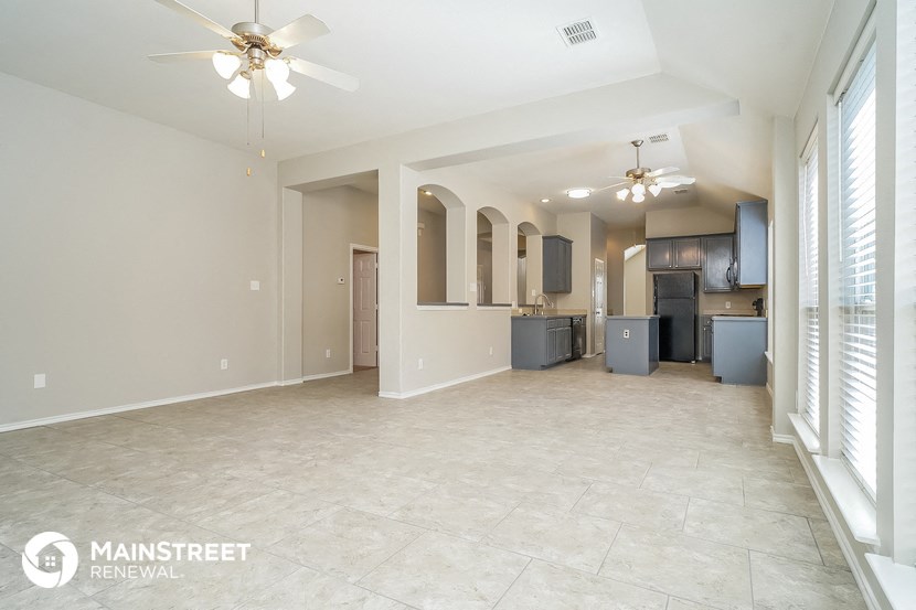 a spacious living room with a kitchen and ceiling fans