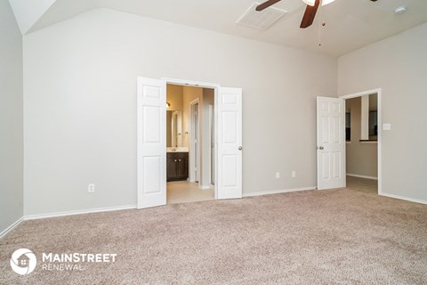 the living room of an apartment with carpet and a ceiling fan