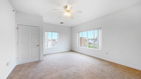 A room with a carpeted floor, a ceiling fan, and two windows.