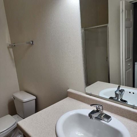 A bathroom with a toilet, sink, mirror and a towel rack.
