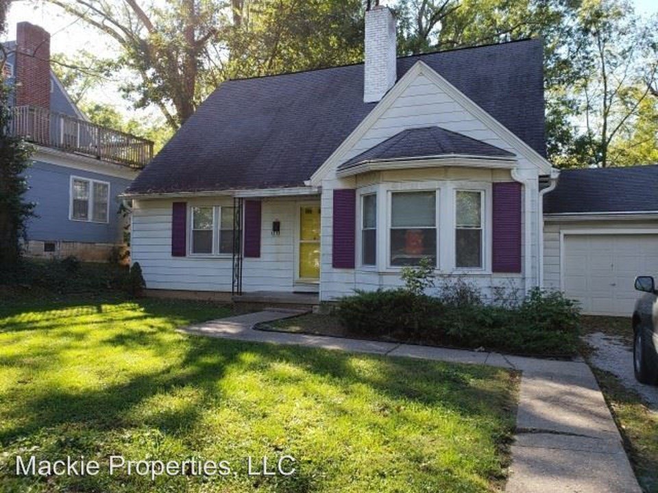 a small white house with purple shutters and a lawn