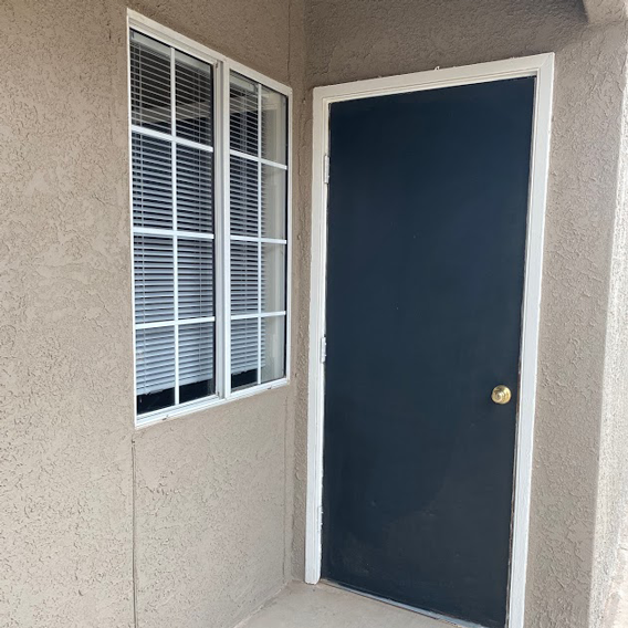 A black door with a gold knob is on the right and a window with white blinds is on the left.