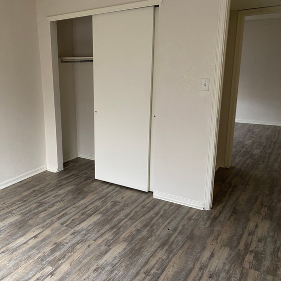 A white closet door is open in a room with wood flooring.