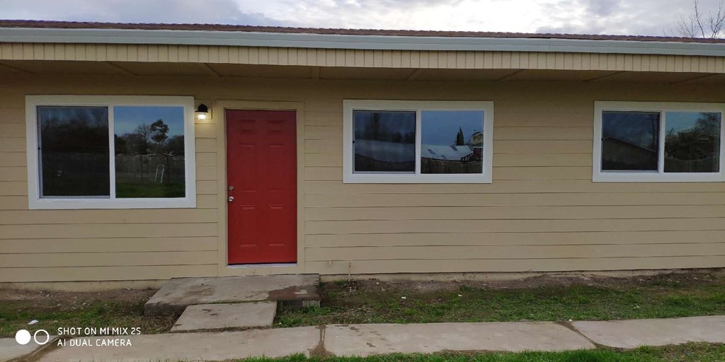the front of a tan house with a red door
