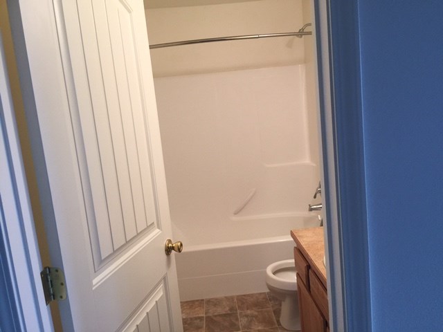 A white door with a gold handle is open to a bathroom with a toilet and a bathtub.