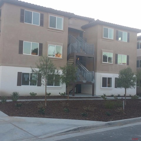 A brown and white building with a balcony and a tree in front.