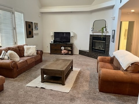 A living room with a brown leather couch, a wooden coffee table, and a fireplace.