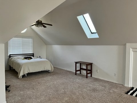 A bedroom with a bed, a table, and a ceiling fan.