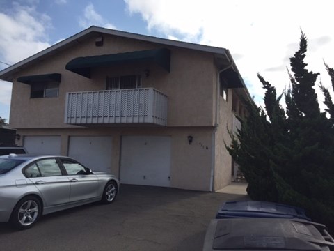 A silver car is parked in front of a house with a balcony.