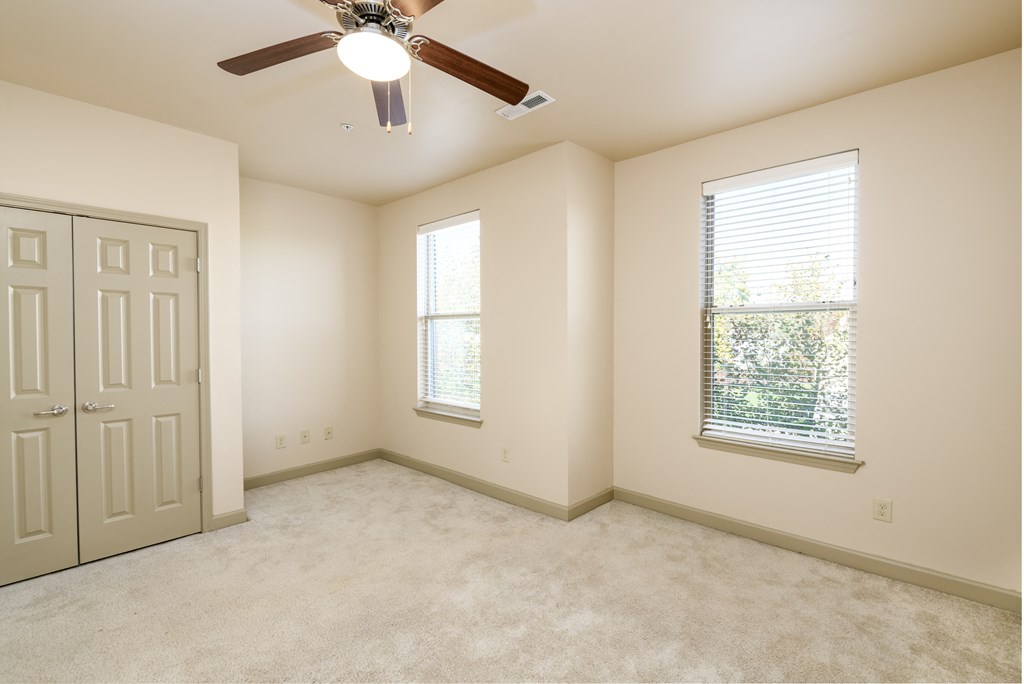 an empty bedroom with a ceiling fan and two windows