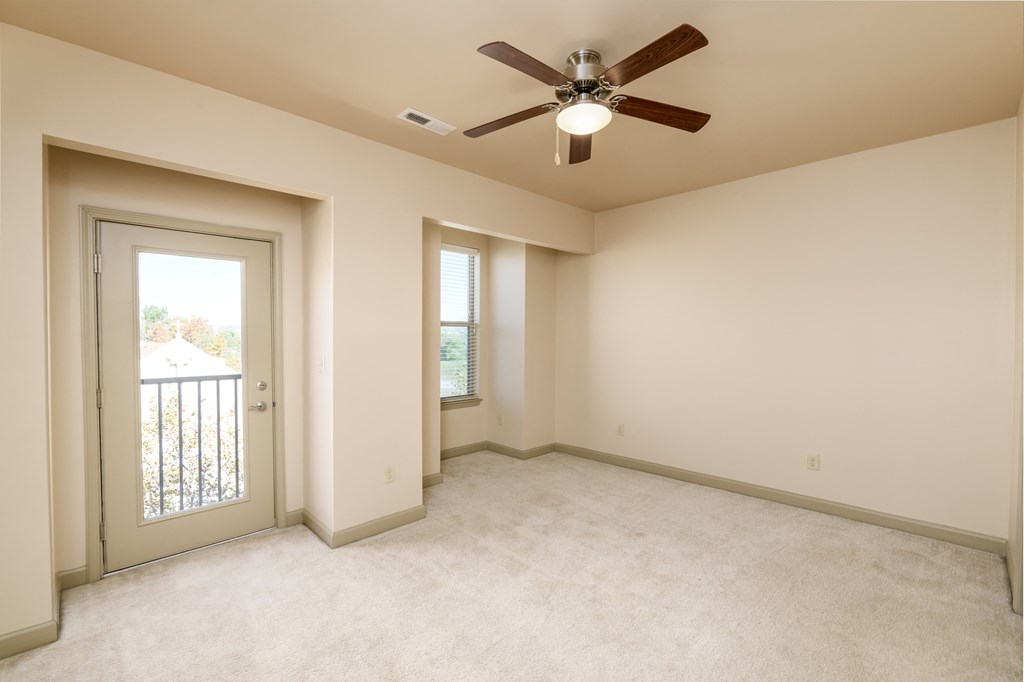 an empty living room with a ceiling fan and a door to a balcony