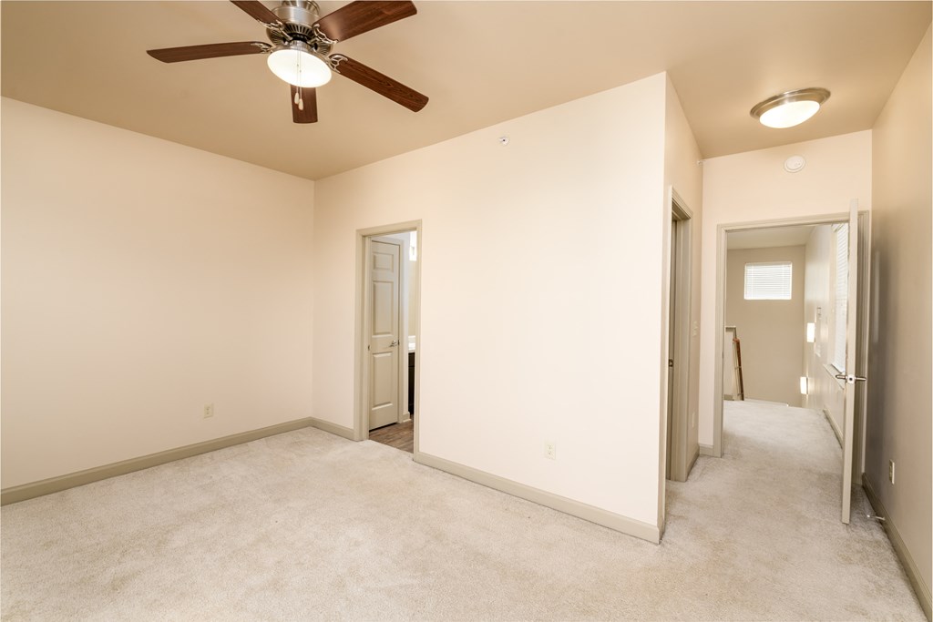 an empty living room with a ceiling fan and a hallway