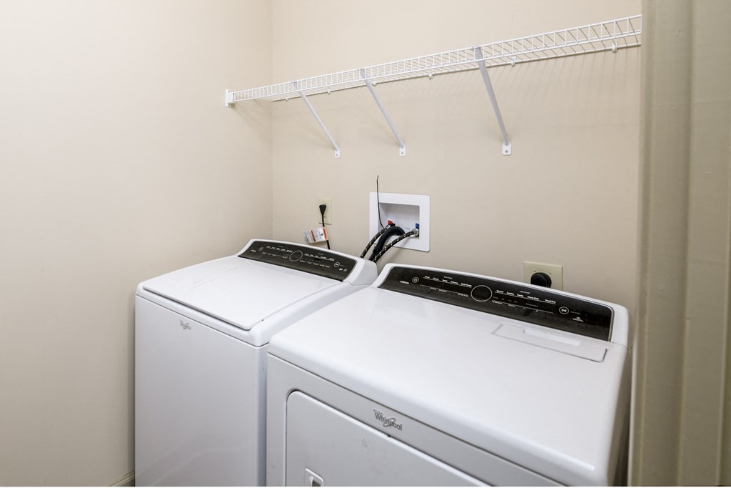 a white washer and dryer in a white room with a white shelf above