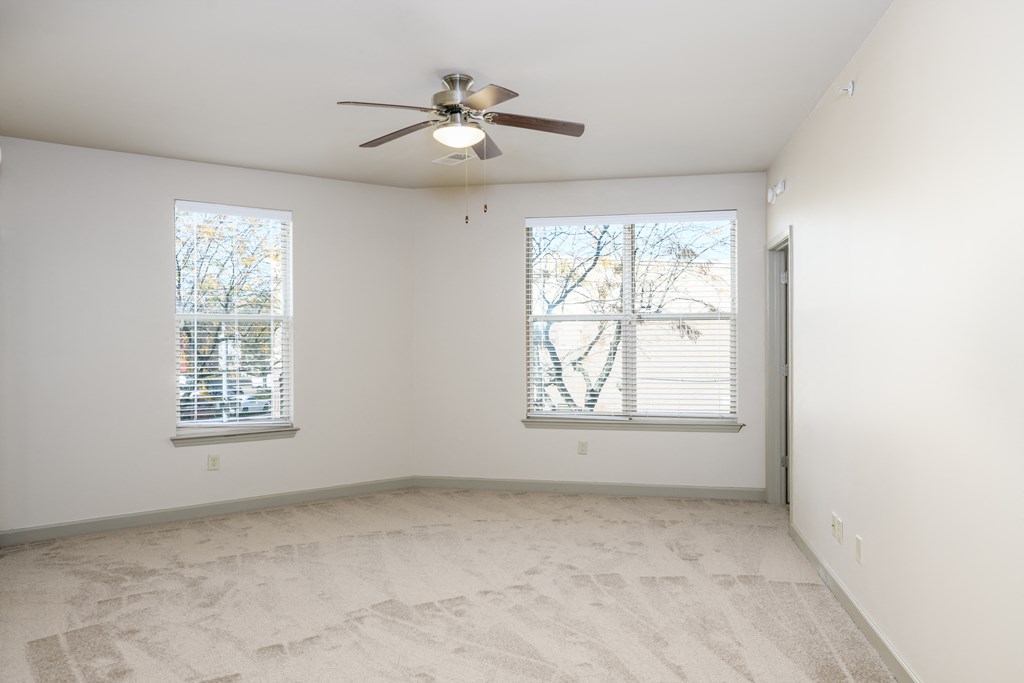 an empty living room with a ceiling fan and two windows