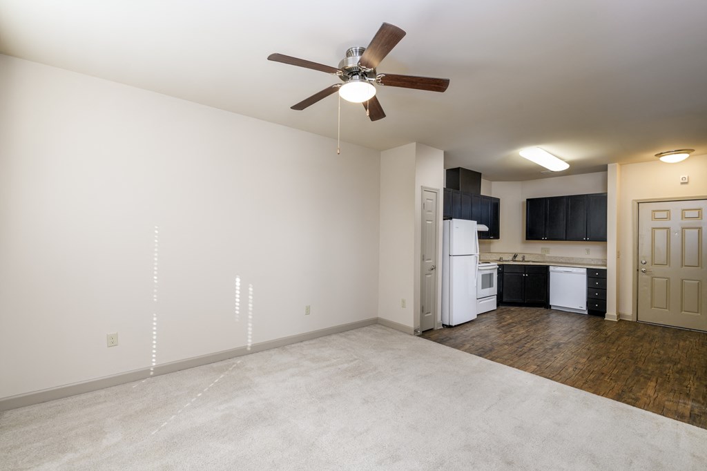 an empty living room with a ceiling fan and a kitchen