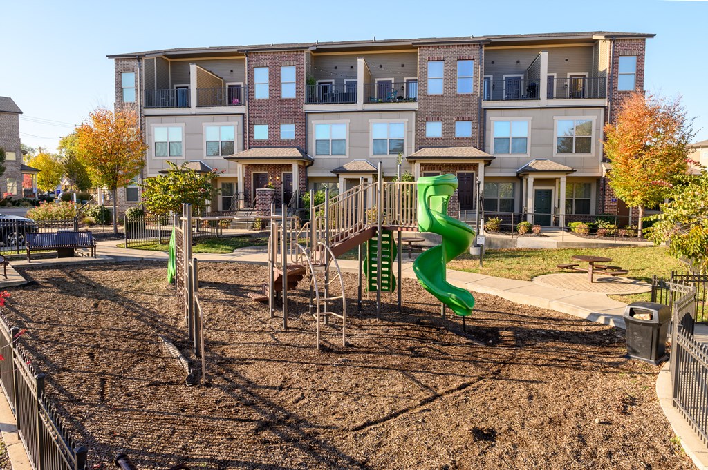 a playground with a green slide in front of an apartment building