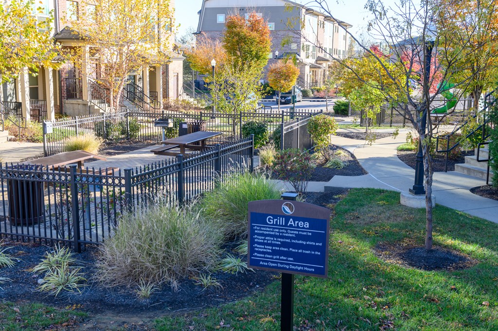 a sign sits in the grass in front of a park and houses