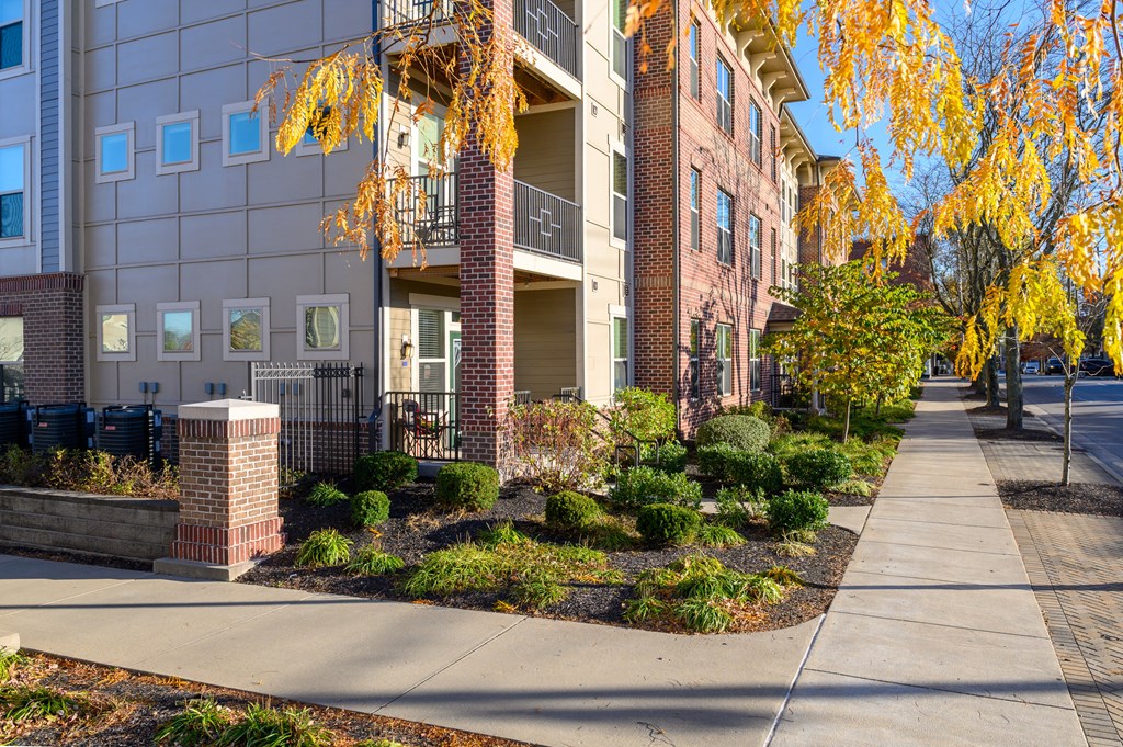an apartment building with a sidewalk and landscaping in front of it