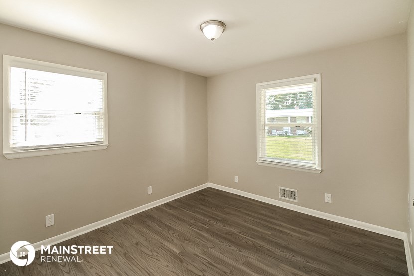 the interior of an empty room with wood flooring and two windows