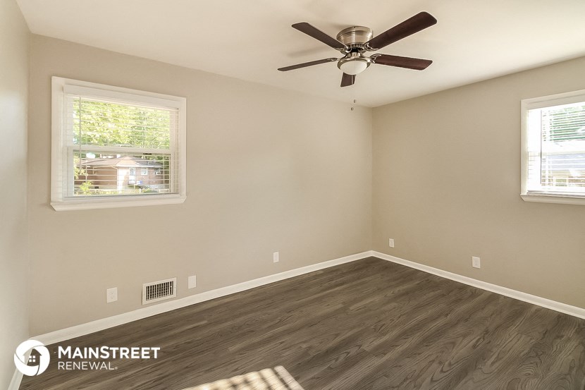 the spacious living room with hardwood flooring and a ceiling fan
