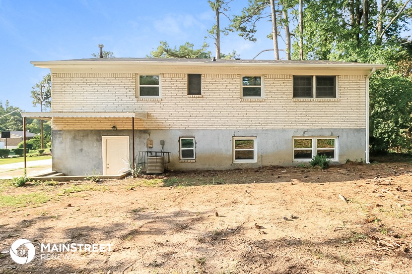 a white brick house with a dirt lot and trees