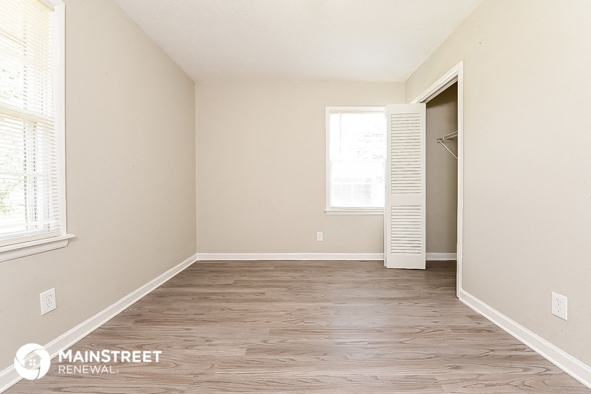 a bedroom with white walls and wood flooring and a closet